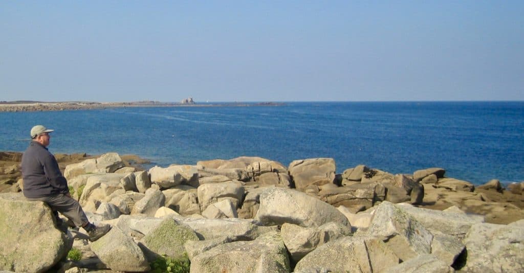 Un homme assis sur les rochers contemple la mer.