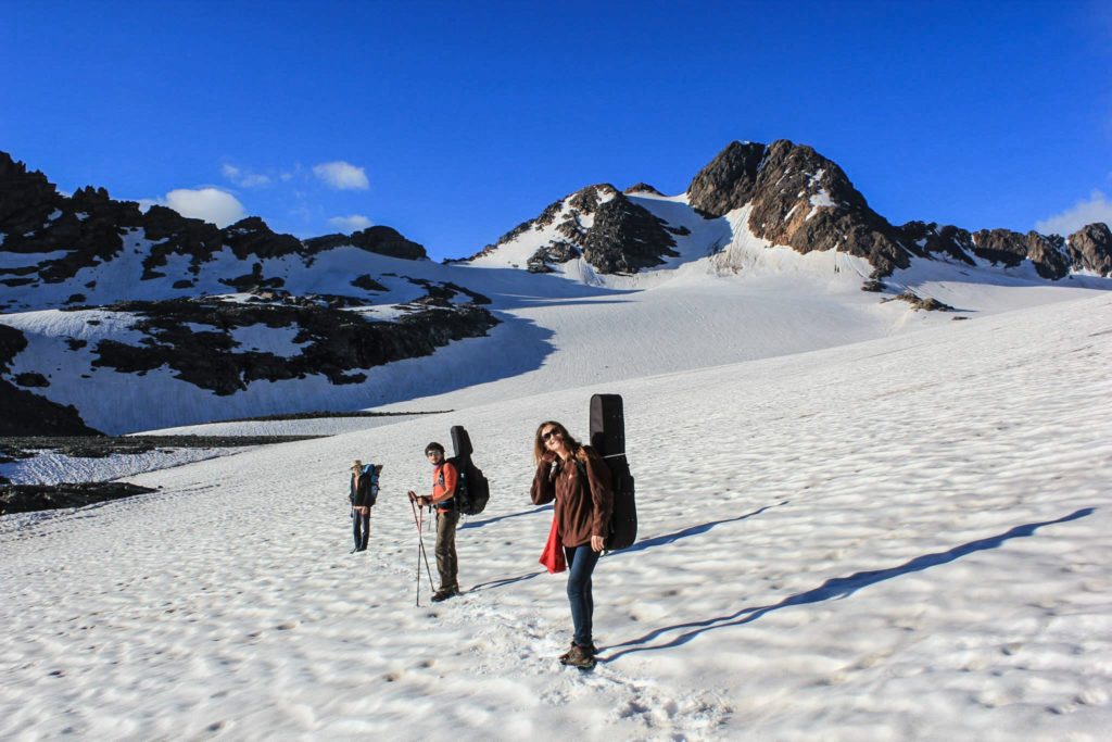 Trois personnes sur la neige enn montagne, avec leurs instruments de musique (deux guitares et une balalaïka) sur le dos.